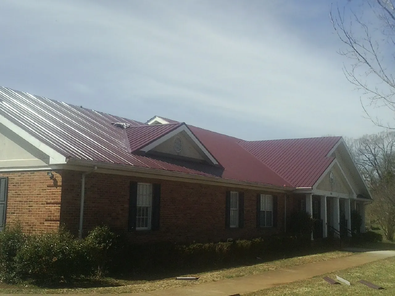 Red metal roof with gabled entries on a long brick building, from a Hail Damage Roof Repair job in Sewanee