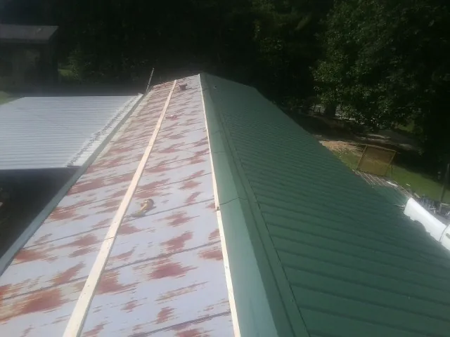 Old rusted panels beside newly installed green metal roofing — Wind Damage Roof Repair by Roofing Brothers in Sewanee