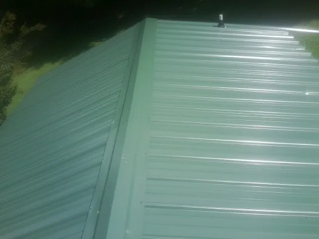 New green metal panels meeting at the ridge of a roof — Flat Roof Repair work by our crew in Sewanee