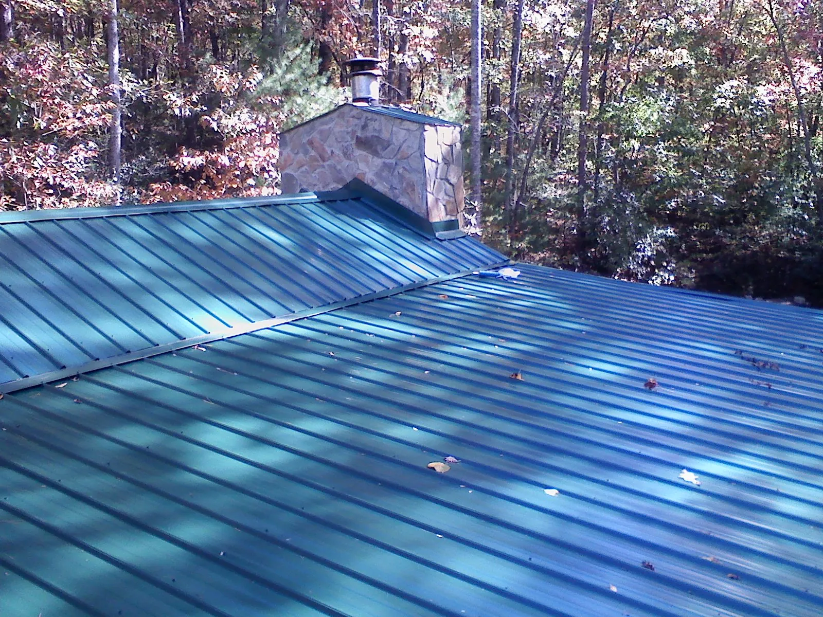 New green metal roof and stone chimney surrounded by autumn woods in Sewanee