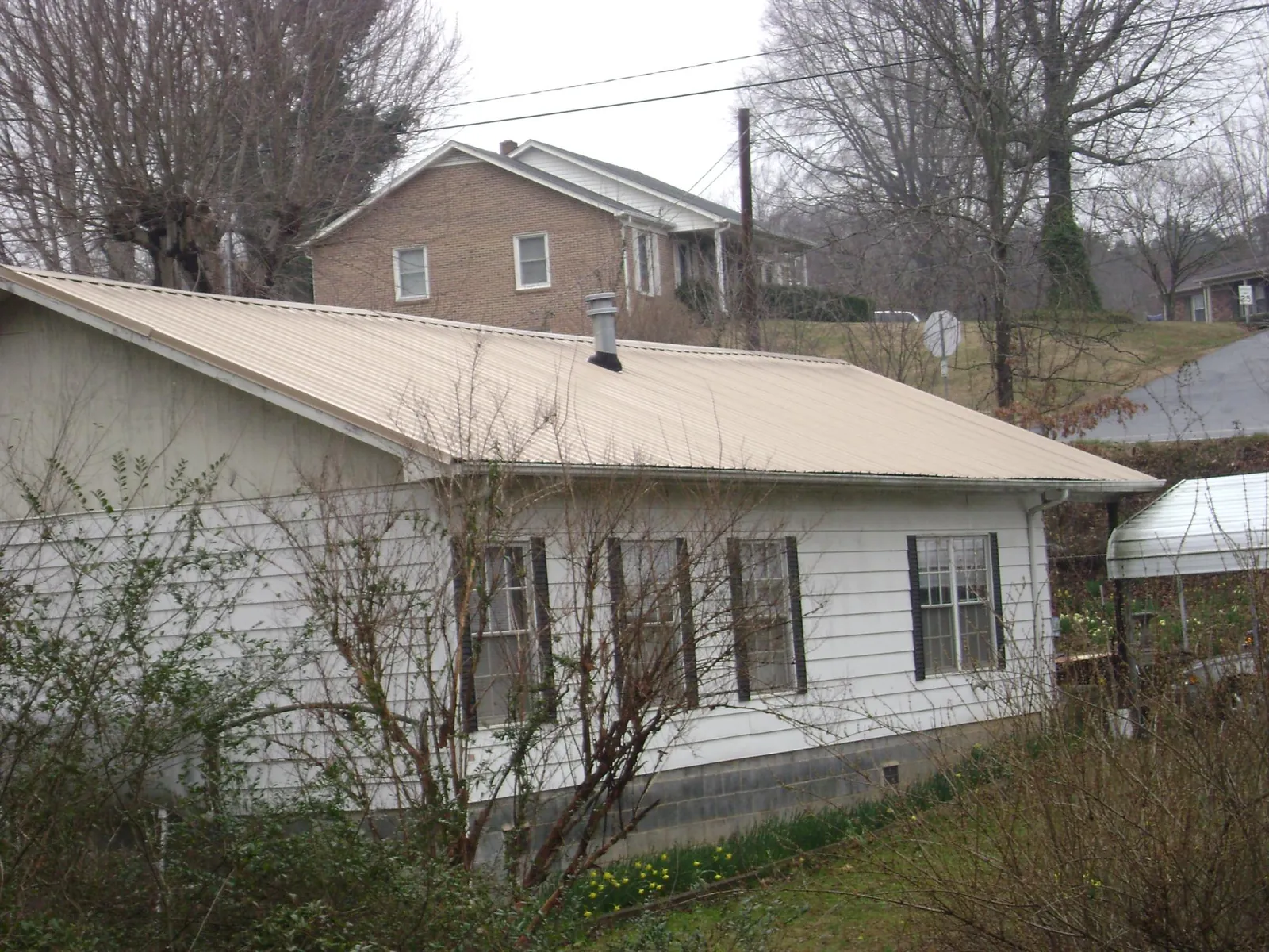 Tan metal roof on a white sided house set into a hillside — Commercial Roofing by Roofing Brothers in Sewanee