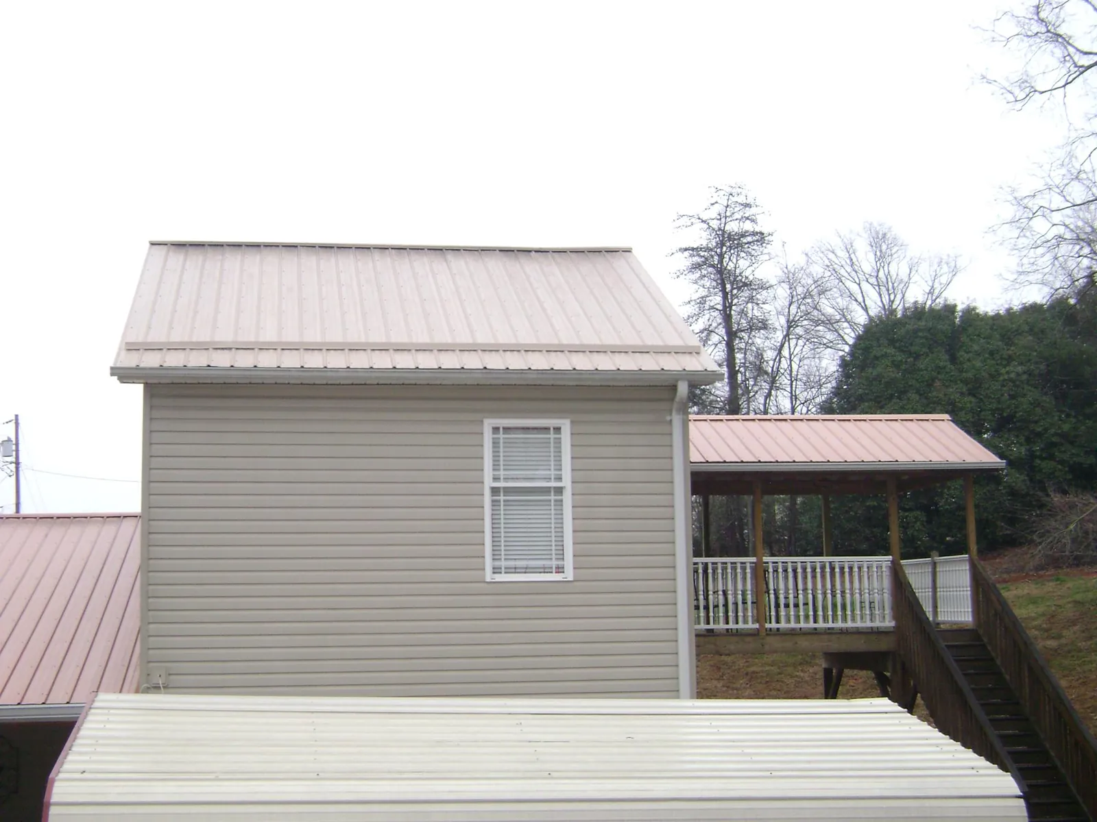 Tan metal roofs on a two story addition and attached porch, from a Roof Replacement job in Sewanee